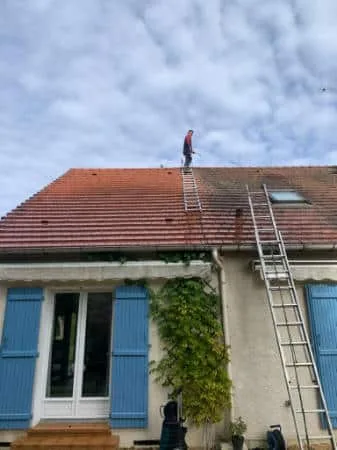 Couvreur sur le faîtage pendant un nettoyage de toiture, la moitié du versant a retrouvé sa couleur d'origine