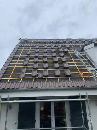Maison en cours de rénovation de toiture, tuiles neuves réparties sur le liteaunage avant la pose